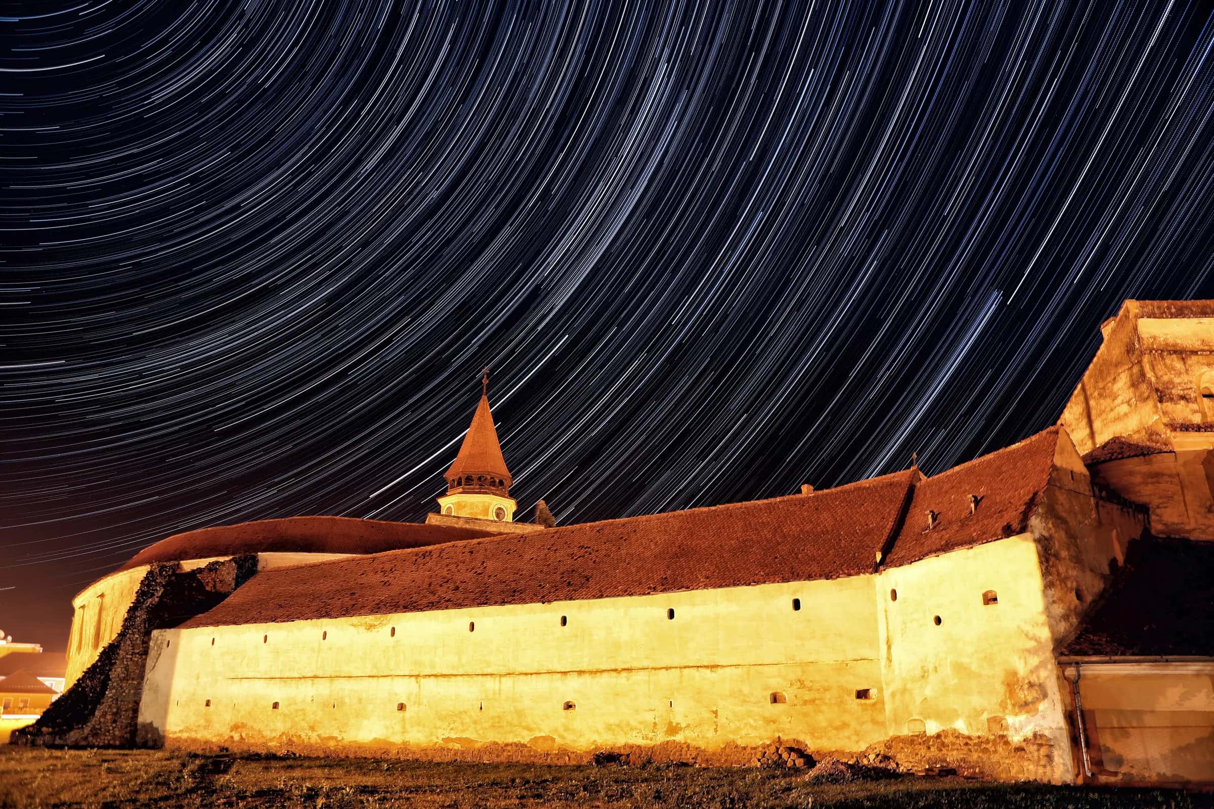 Scie di stelle sopra le mura illuminate della chiesa fortificata di Prejmer, di notte
