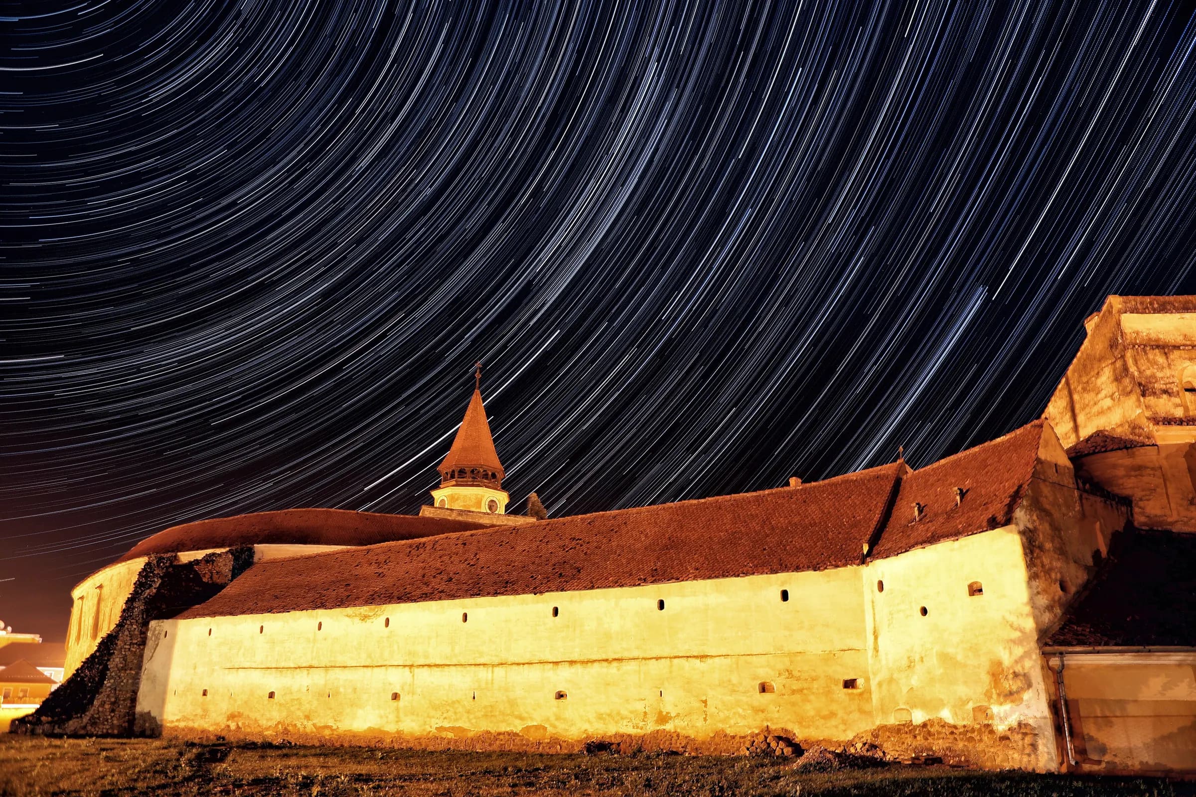 Traiectorii de stele peste zidurile luminate ale bisericii fortificate din Prejmer, noaptea